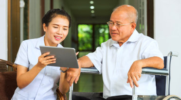 elder man sitting on a wheelchair looking to the tablet with caregiver